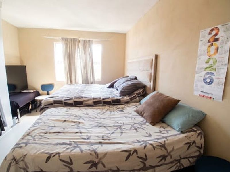 A bedroom featuring an upholstered headboard and curtain rails, with walls showing signs of wear and uneven texture.