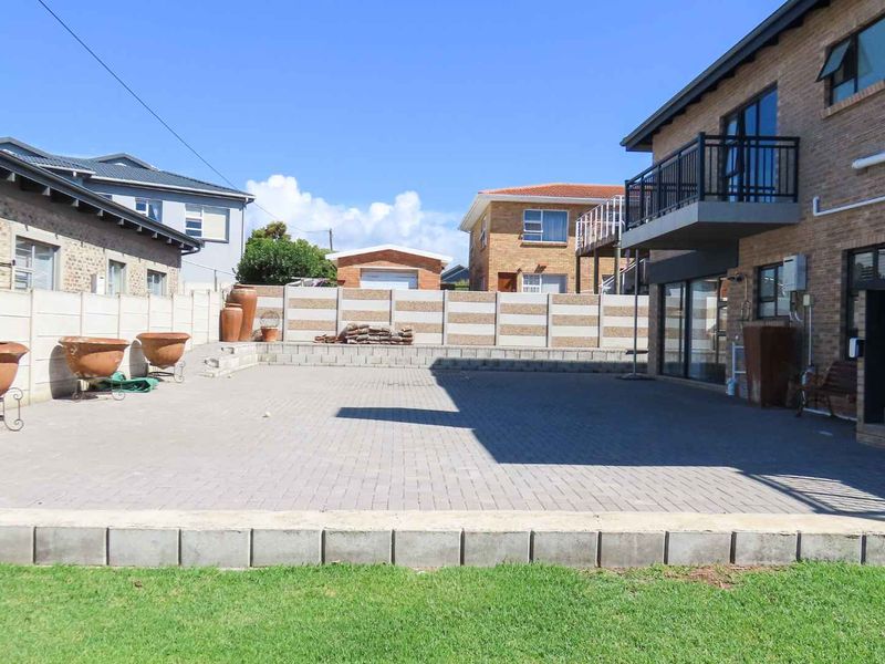 Spacious paved rear patio area featuring a brick facade, balcony access, and secure precast concrete boundary walls.