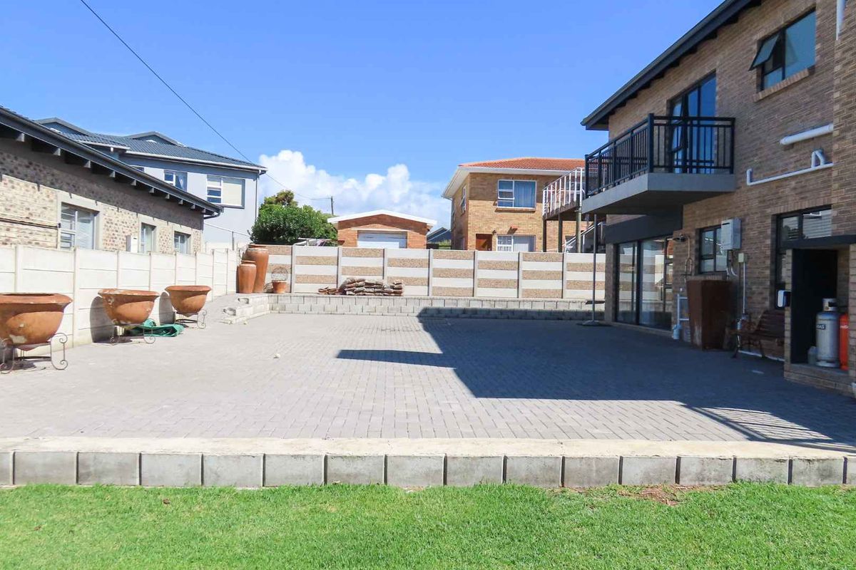 Spacious paved rear patio area featuring a brick facade, balcony access, and secure precast concrete boundary walls.