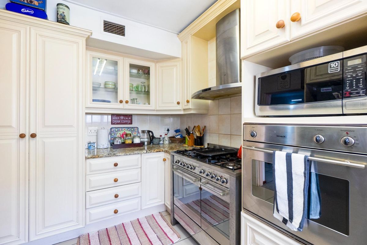 A functional kitchen featuring cream-colored cabinetry, granite countertops, a stainless steel gas stove with extractor fan, and a built-in oven and microwave unit.