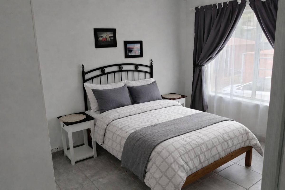A well-maintained bedroom featuring neutral tiled flooring and large windows with installed curtain rails, providing a bright and comfortable living space.
