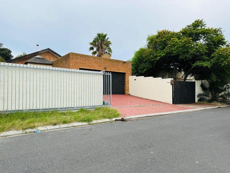 Front exterior view of the property featuring a brick facade, single garage, paved driveway, and secure perimeter wall with metal gate.