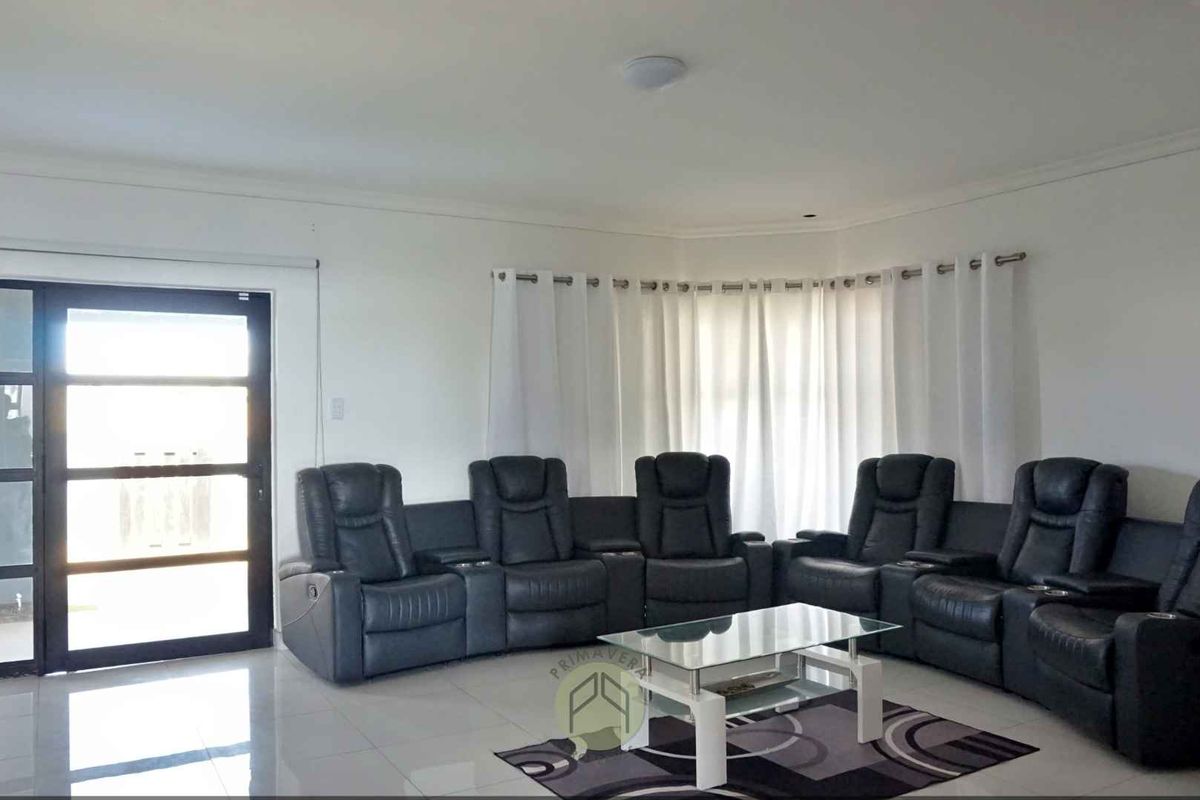 A spacious living room featuring large format floor tiles, a modern glass-paneled door, and expansive windows with fitted curtain tracks.