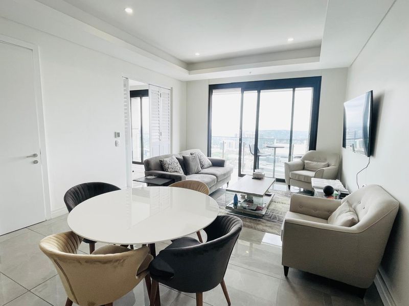 Bright open-plan living and dining area featuring tiled floors, recessed ceiling lighting, and large sliding glass doors leading to a balcony with city views.