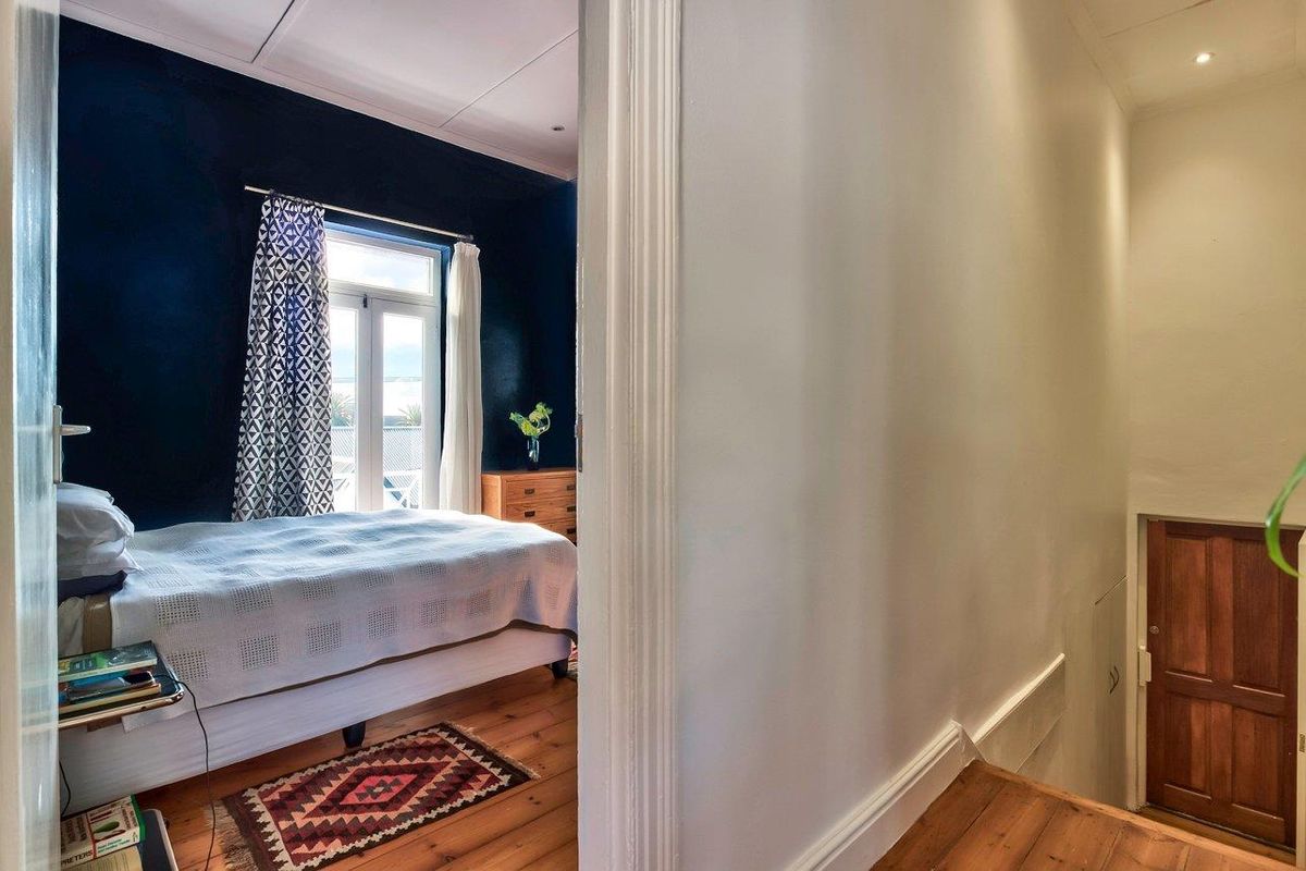A view from a hallway looking into a bedroom featuring dark accent walls, timber flooring, and a glass door leading to an outdoor area.