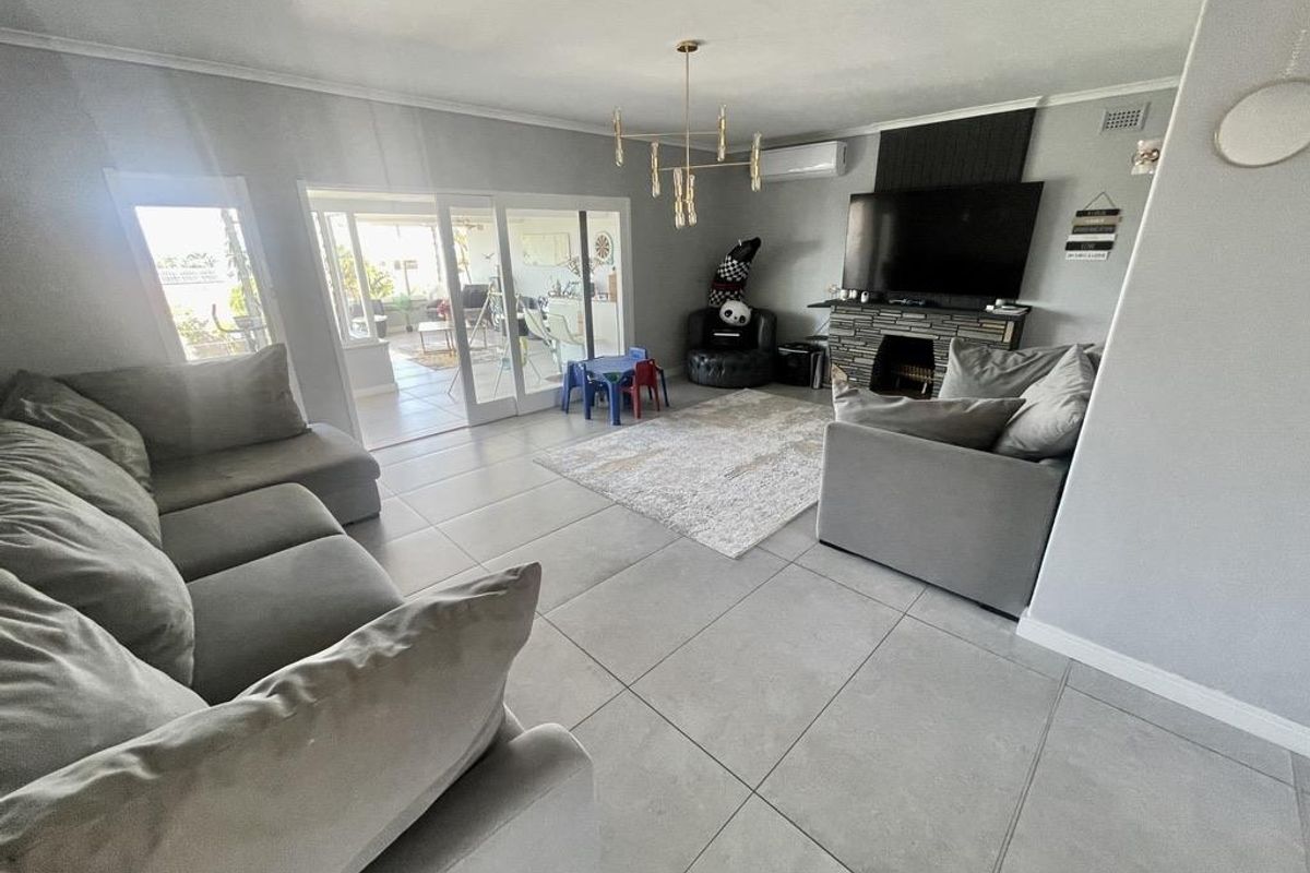 Spacious living room featuring large format floor tiles, a stone-clad fireplace, and sliding glass doors providing seamless access to the outdoor patio area.