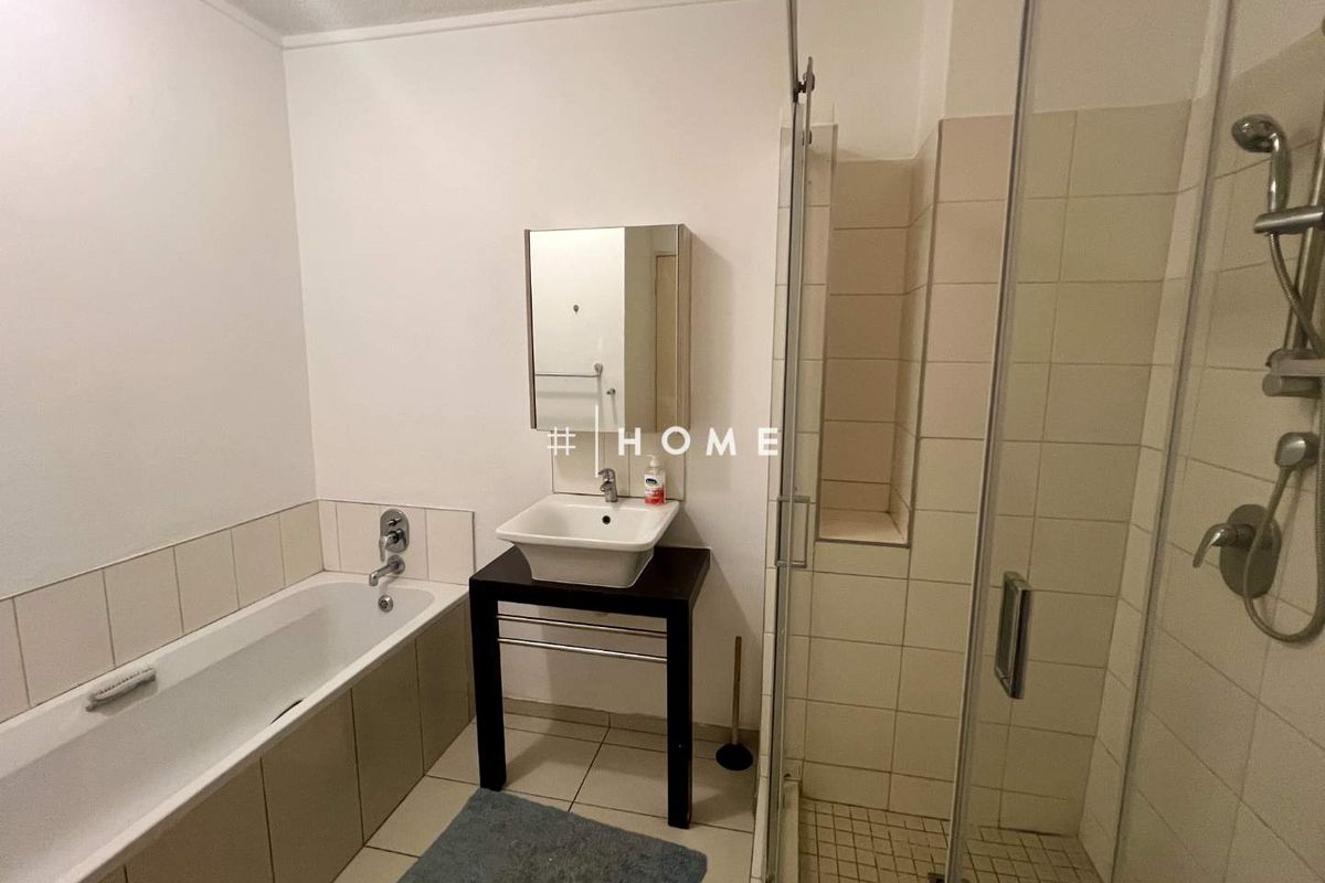 A functional bathroom featuring a separate bathtub and shower enclosure, vessel sink vanity, and neutral wall tiling.