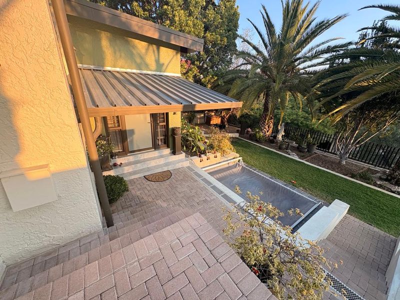 Rear exterior view featuring a paved patio area, a covered swimming pool, and a metal awning over the entrance.