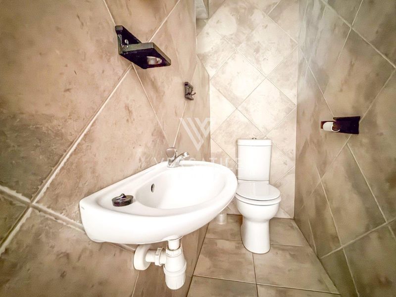 A compact bathroom featuring tiled walls and flooring, equipped with a wall-mounted basin and a standard toilet.