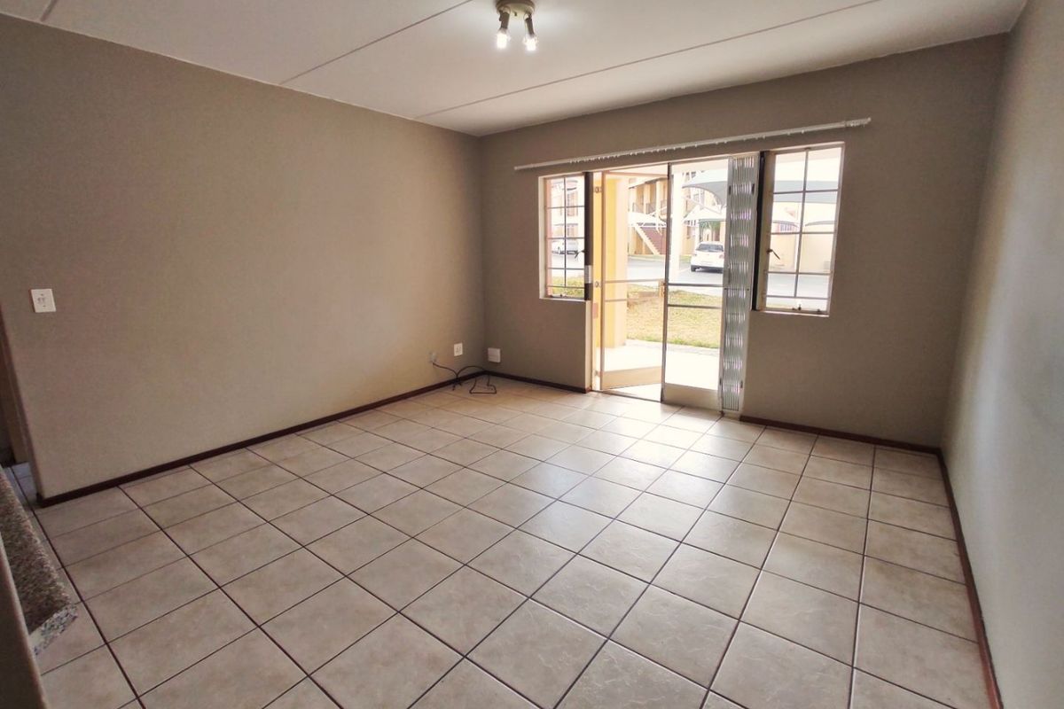 An empty, well-lit living room featuring neutral tiled flooring and a sliding glass door providing access to the exterior.