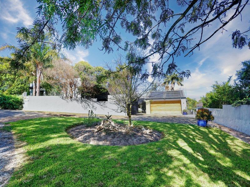Front exterior view of the property featuring a landscaped lawn, boundary wall, and a garage equipped with solar panels.