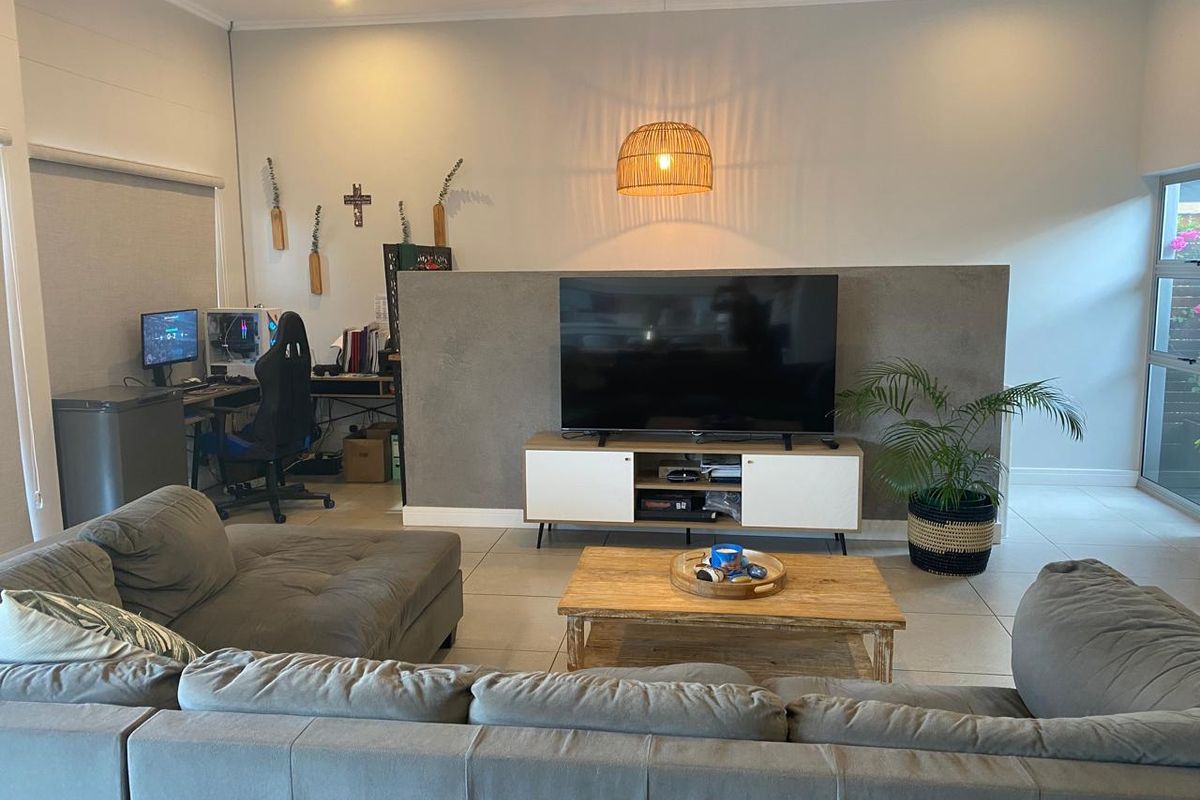 A modern living room featuring tiled flooring, recessed lighting, and a central partition wall creating a functional space for relaxation and a home office area.