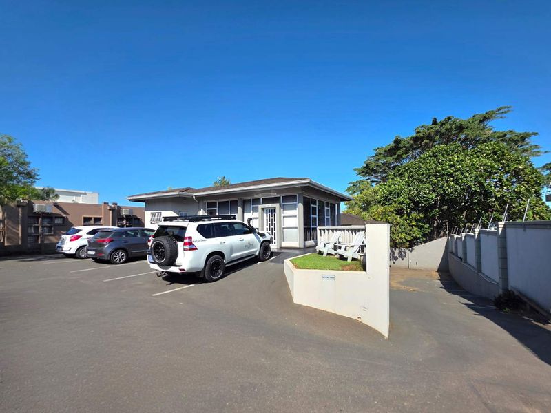 Front exterior view of the business premises featuring a paved parking area, perimeter security wall, and landscaped garden bed.