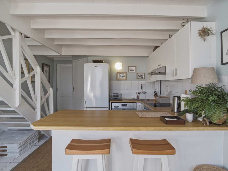 Open-plan kitchen featuring a breakfast bar, white cabinetry, and exposed ceiling beams, seamlessly integrated with the staircase area.