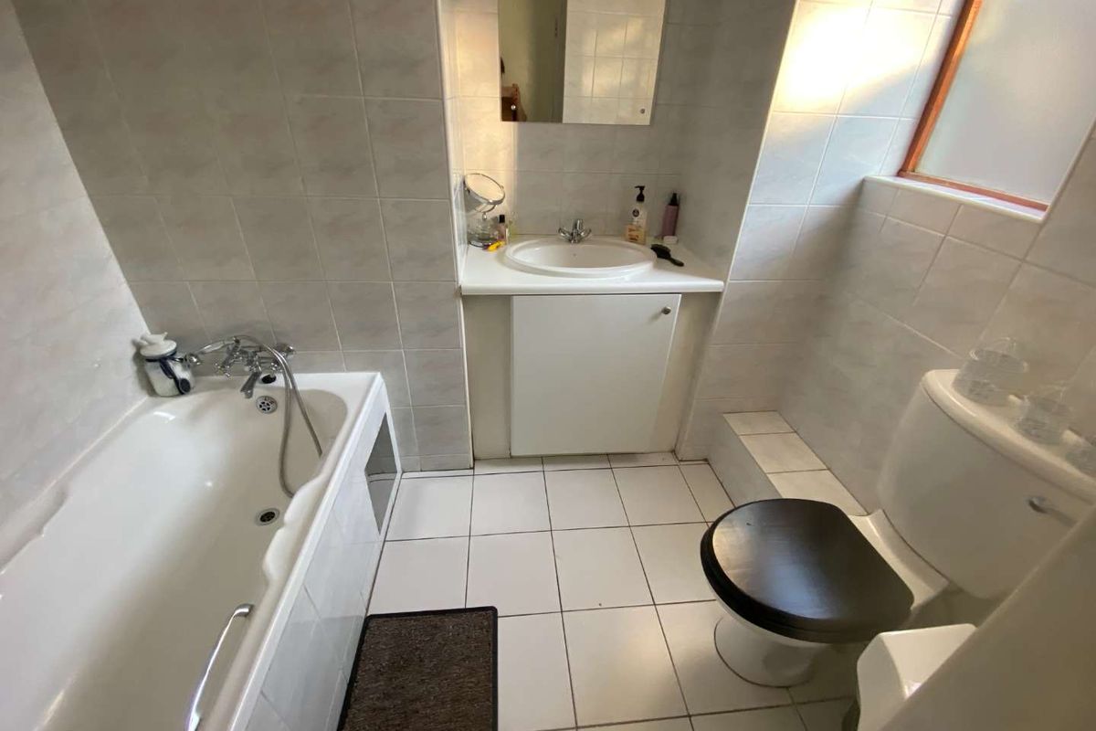 A functional bathroom featuring a built-in vanity with a ceramic basin, a standard bathtub, and a toilet, finished with neutral wall and floor tiles.