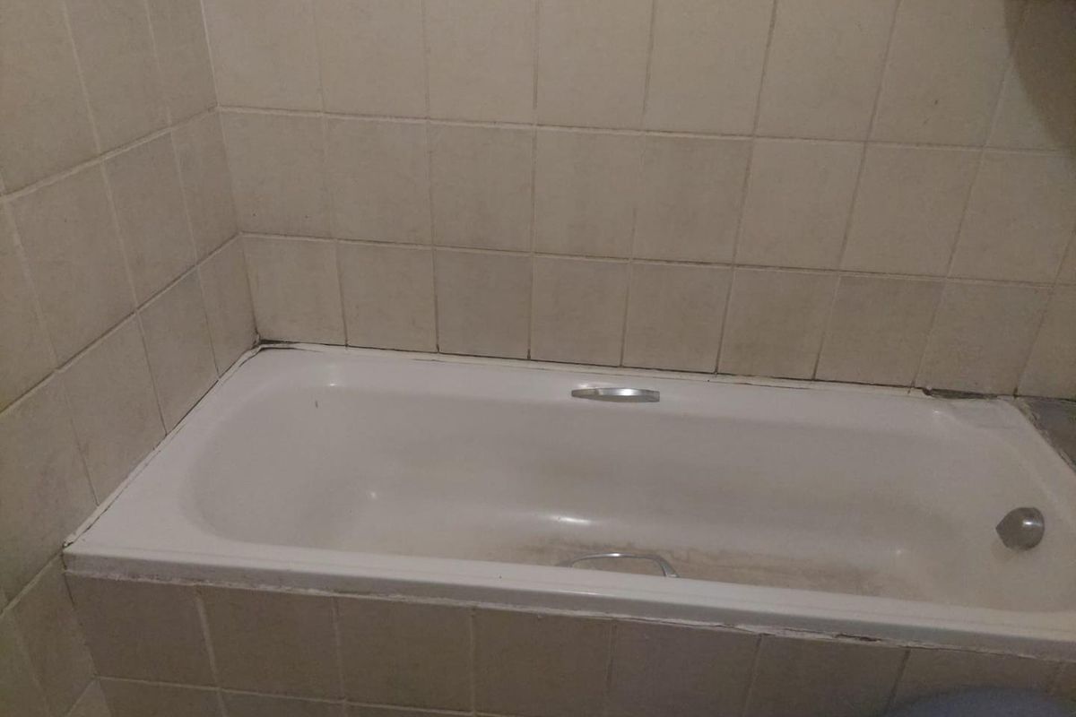 A bathroom featuring a built-in bathtub with tiled surround, requiring maintenance to the grout and sealant.