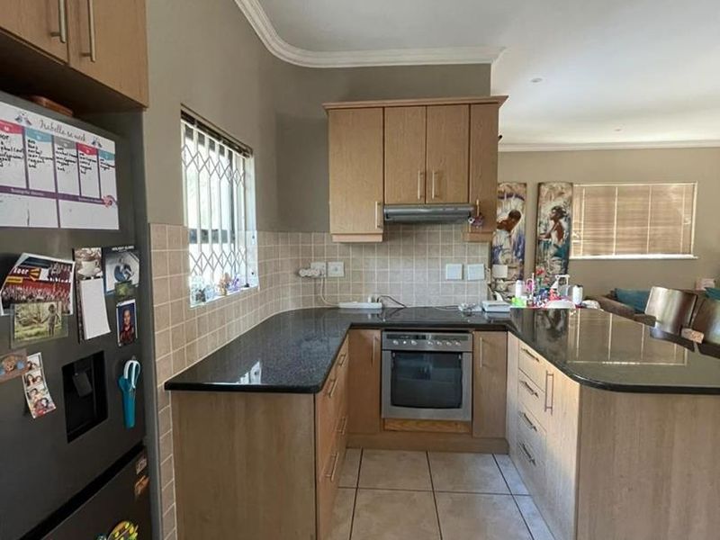 Functional kitchen featuring light wood cabinetry, dark granite countertops, built-in oven, extractor fan, and neutral ceramic floor tiles.