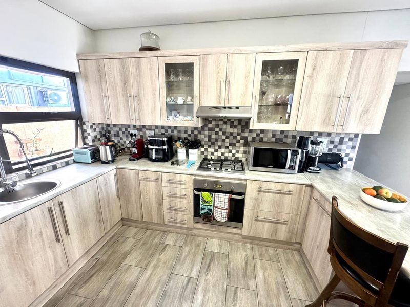 A well-maintained kitchen featuring light wood-look cabinetry, a gas hob, built-in oven, extractor fan, and a modern tiled backsplash.
