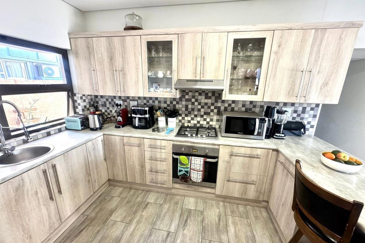 A well-maintained kitchen featuring light wood-look cabinetry, a gas hob, built-in oven, extractor fan, and a modern tiled backsplash.