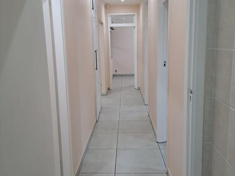 A clean, neutral-toned hallway featuring large format floor tiles, recessed lighting, and integrated storage cupboards, providing access to multiple rooms.