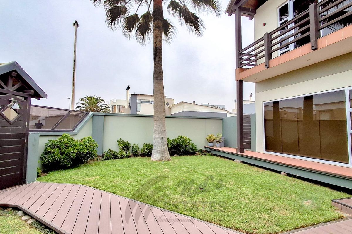 A well-maintained rear garden featuring timber decking, a manicured lawn, boundary walls, and direct access to the home via large sliding glass doors.