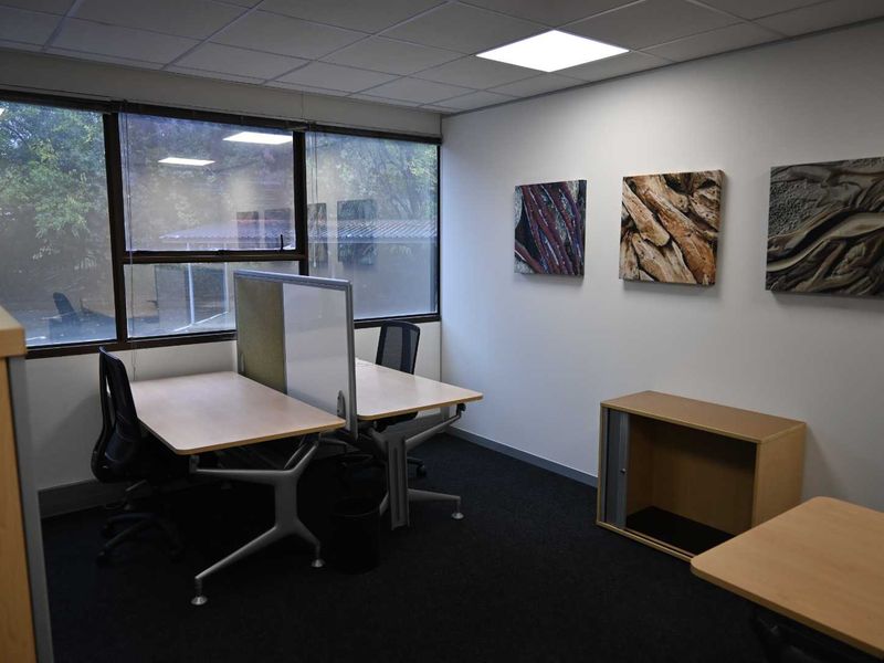 A functional office space featuring a suspended ceiling with recessed LED lighting, large windows providing natural light, and dark carpet flooring.