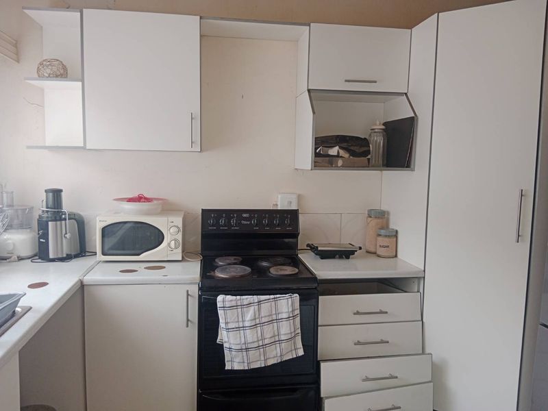 A compact kitchen featuring white cabinetry, laminate countertops, a tiled backsplash, and a freestanding stove, offering a functional layout with potential for cosmetic updates.
