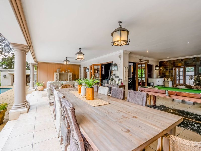 Spacious covered patio featuring tiled flooring, stone columns, and a stone feature wall, overlooking the swimming pool area.