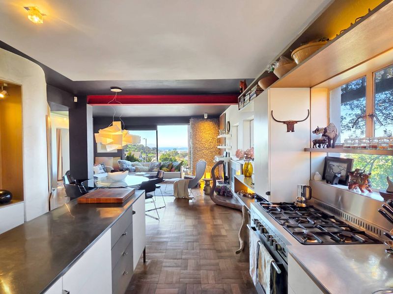 Spacious open-plan living area featuring a modern kitchen with gas cooktop, parquet flooring, and an exposed structural beam, leading to a scenic view.