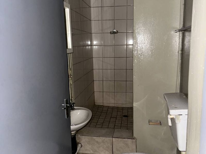 A compact, dated bathroom featuring a tiled shower area, wall-mounted basin, and toilet, requiring modernization and cosmetic updates.