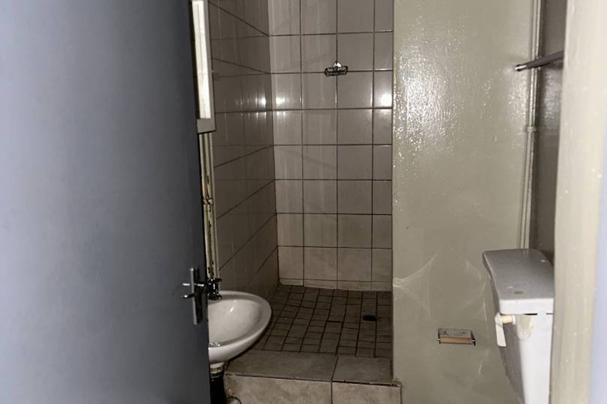 A compact, dated bathroom featuring a tiled shower area, wall-mounted basin, and toilet, requiring modernization and cosmetic updates.