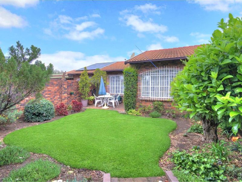 A private rear garden featuring a well-maintained lawn, paved patio area, and brick boundary wall, complemented by established landscaping and security window bars.