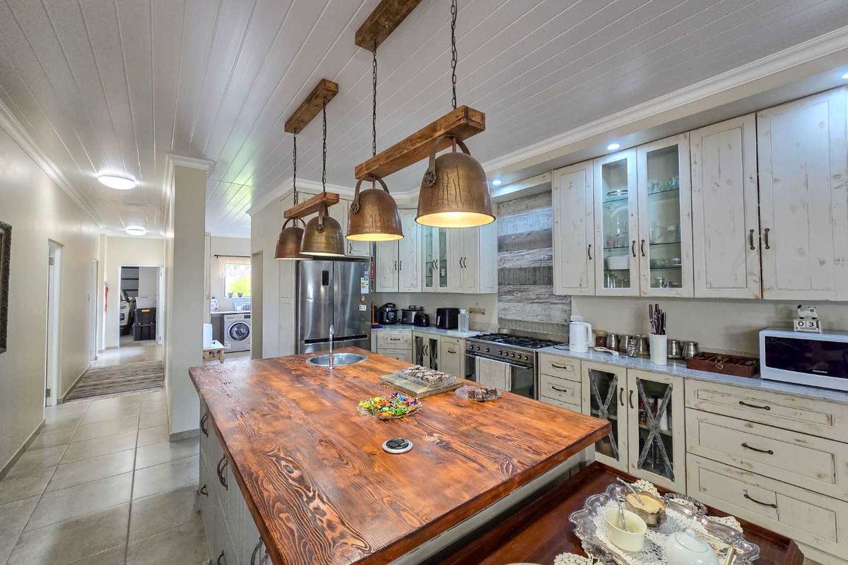 Spacious kitchen featuring a large wooden island, rustic pendant lighting, white cabinetry, and a tiled floor, with an adjacent laundry area visible.