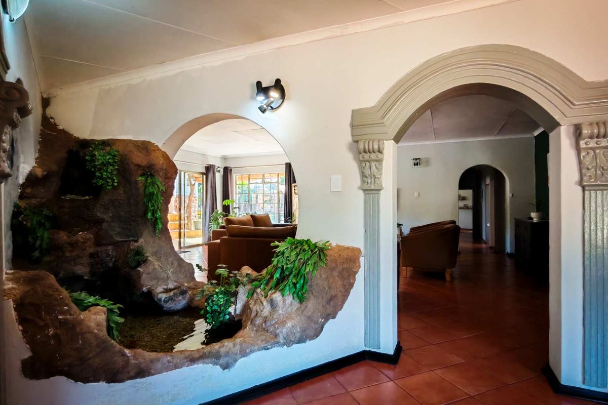 Interior view featuring a unique built-in rock water feature, decorative arched doorways with ornate corbels, and terracotta floor tiling connecting living spaces.