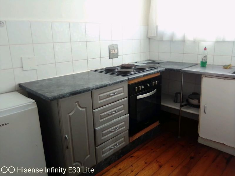 A compact kitchen featuring built-in oven and hob, laminate countertops, tiled backsplash, and timber flooring, offering potential for a modern renovation.