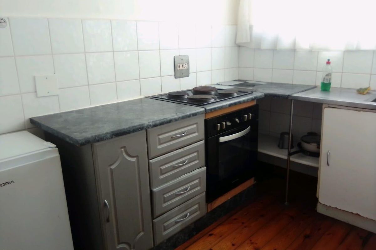 A compact kitchen featuring built-in oven and hob, laminate countertops, tiled backsplash, and timber flooring, offering potential for a modern renovation.