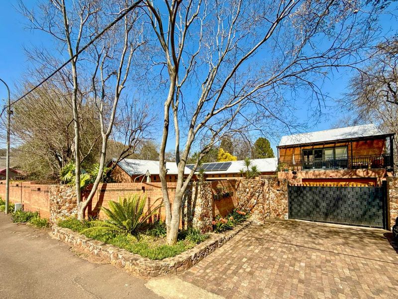 Front exterior view of the property featuring a brick and stone boundary wall, paved driveway, secure metal gate, and a balcony with a metal roof.