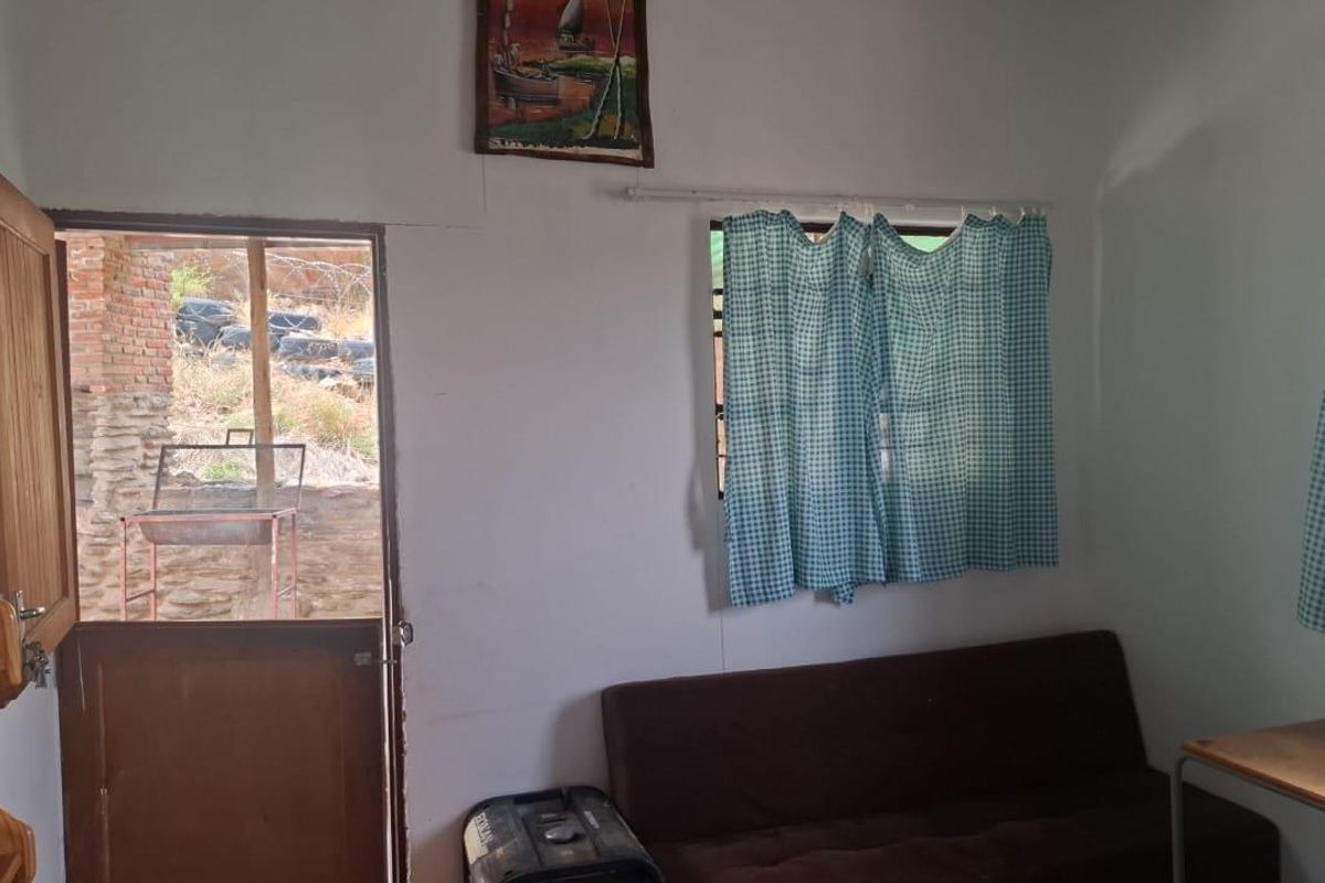 A simple bedroom featuring a timber door leading to an outdoor area and a window with security bars.