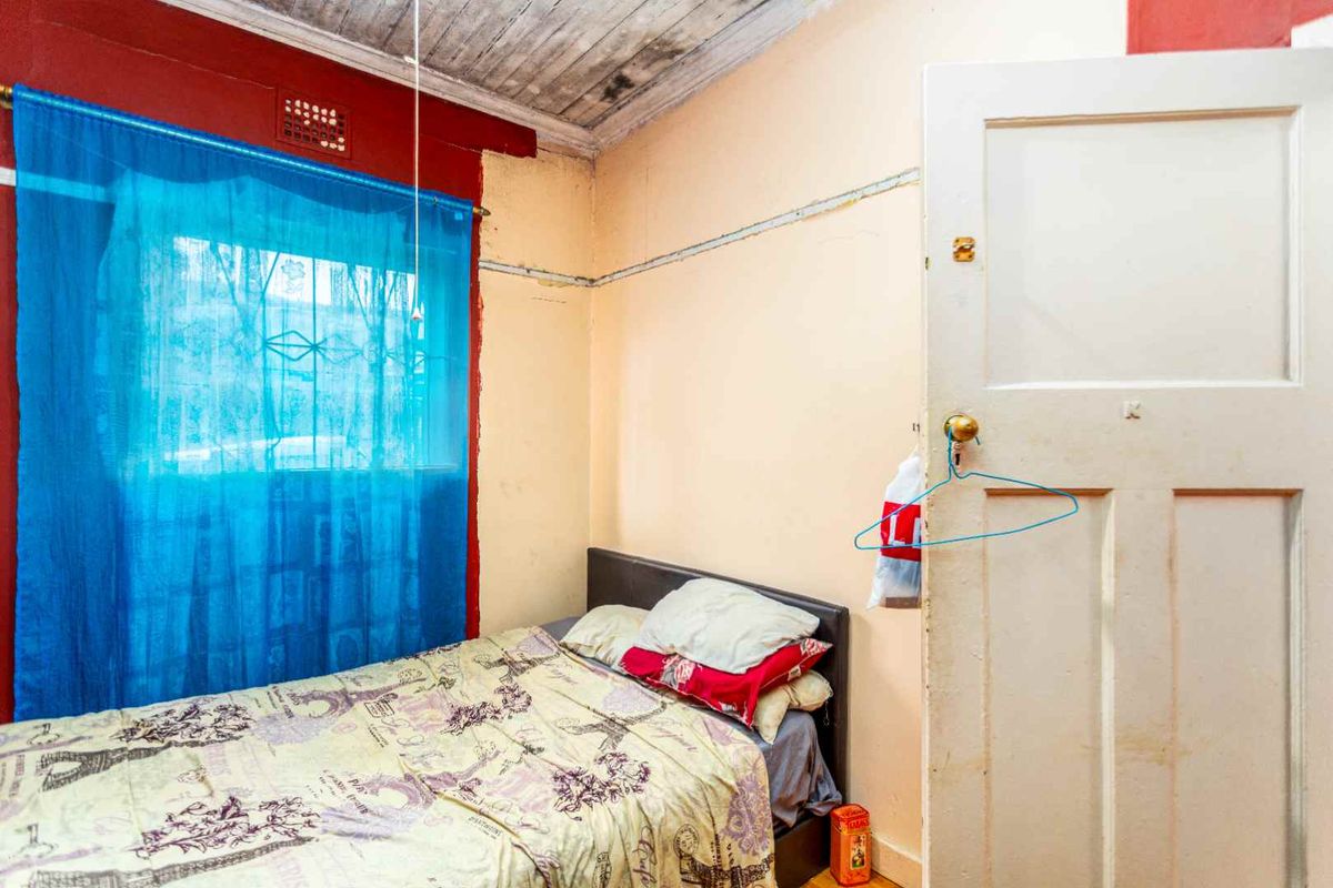 A bedroom featuring a timber ceiling, security bars on the window, and a traditional panel door, requiring cosmetic updates and maintenance.