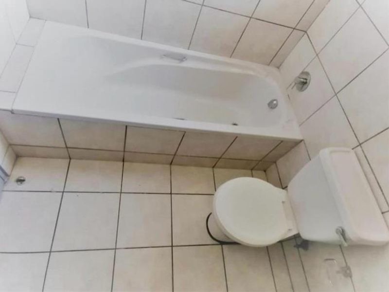 A functional bathroom featuring a built-in bathtub and a standard toilet with tiled walls and flooring throughout.