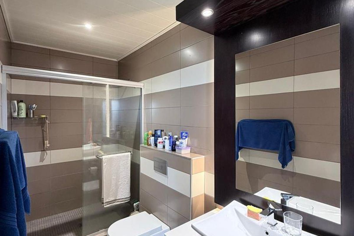 Modern bathroom featuring a glass-enclosed shower, wall-mounted toilet, and a contemporary vanity with a vessel sink and integrated mirror lighting.