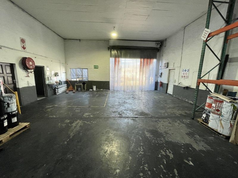 Spacious industrial warehouse unit featuring high ceilings, concrete flooring, a large roller shutter door with PVC strip curtains, and integrated storage racking.
