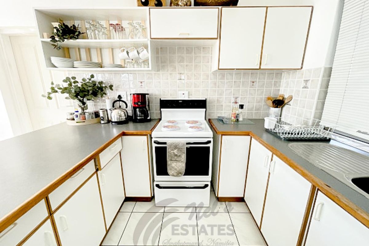A functional kitchen featuring white cabinetry, laminate countertops, a freestanding stove, and tiled flooring, offering a practical layout for daily meal preparation.