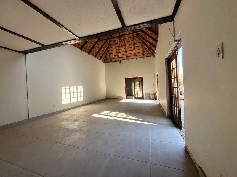 Spacious, empty living area featuring a high thatched ceiling with exposed beams, tiled flooring, and multiple timber-framed glass doors leading to the exterior.