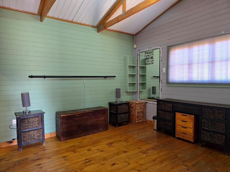 A bedroom featuring timber flooring, exposed rafters, and painted timber wall cladding, complemented by built-in shelving and window blinds.