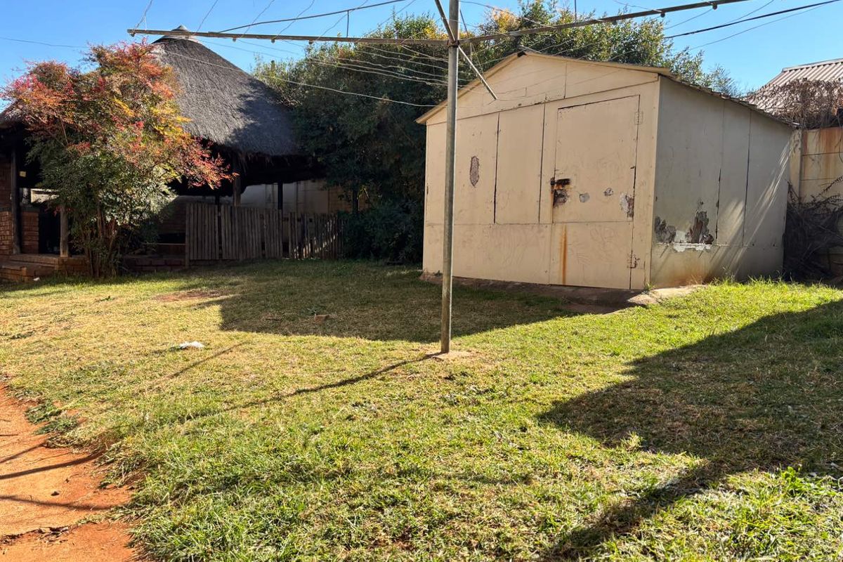 Rear garden area featuring a thatched lapa, a metal storage shed, and a rotary clothesline set within a grassed yard.