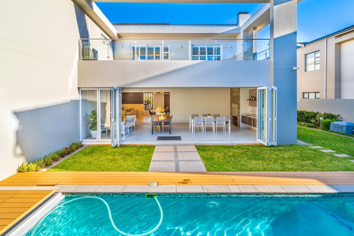 Modern rear elevation featuring a swimming pool with timber decking, a spacious covered patio with bi-fold doors, and a built-in braai area.