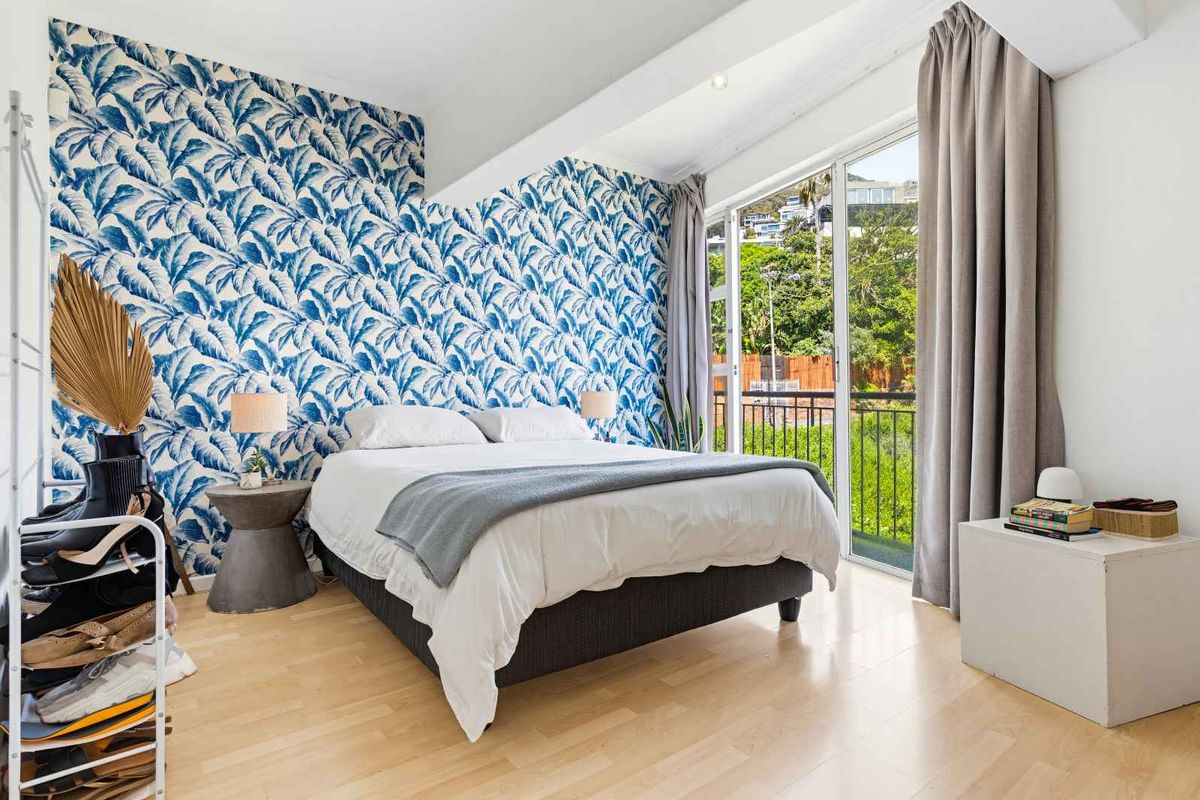 Bright bedroom featuring laminate flooring, bold patterned wallpaper, and a sliding glass door providing direct access to a private balcony.