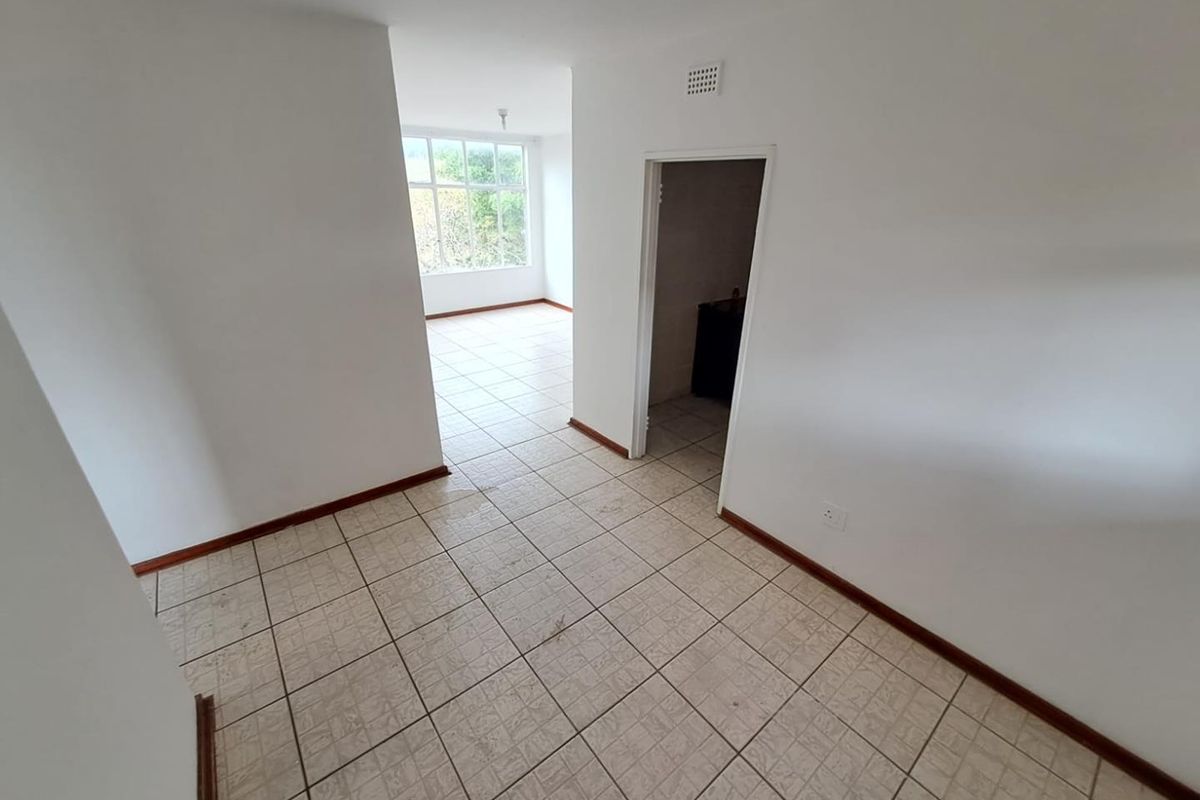 An empty, open-plan living area featuring neutral white walls, tiled flooring, and natural light from a large window.