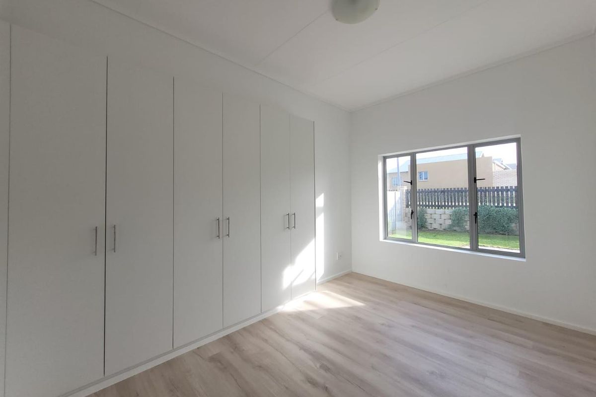 A bright, empty bedroom featuring light wood-look flooring, built-in floor-to-ceiling wardrobes, and a large window overlooking the rear garden.